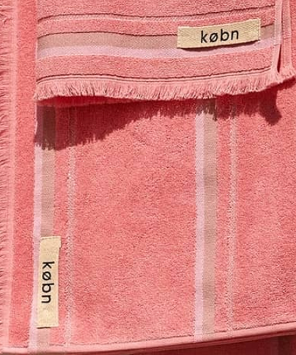 Two soft pink towels with striped design and fabric labels, one larger towel folded over a smaller one.