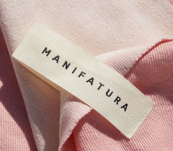 Custom cotton label in cream with black lettering, featuring the word "MANIFATURA," placed on soft pink fabric.