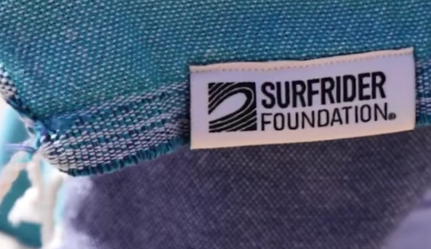 "Rectangular fabric label in white with blue logo and black text, stitched onto a textured blue and gray fabric."