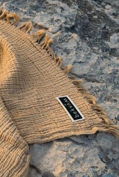 "Tan cotton label with fringed edges on textured gray rock surface, featuring a black and white tag."